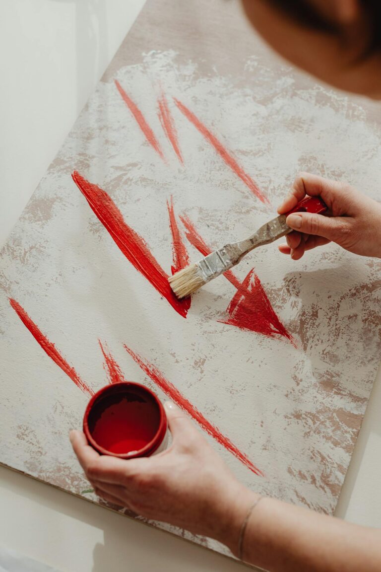 Artist painting bold red strokes on canvas, showcasing creativity and artistic expression.
