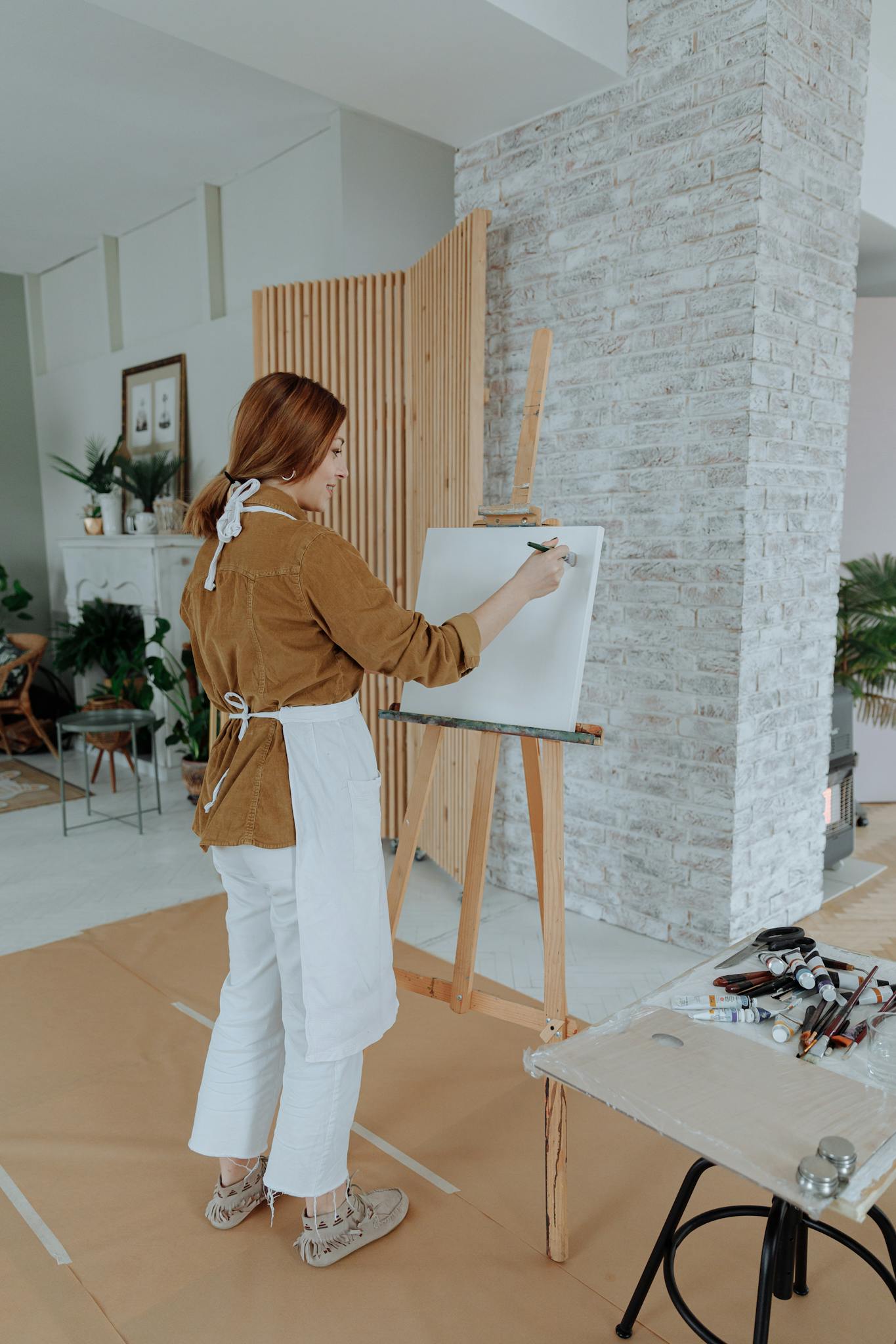 Artist painting on canvas in a well-lit home studio interior with an easel, perfect for creative inspiration.