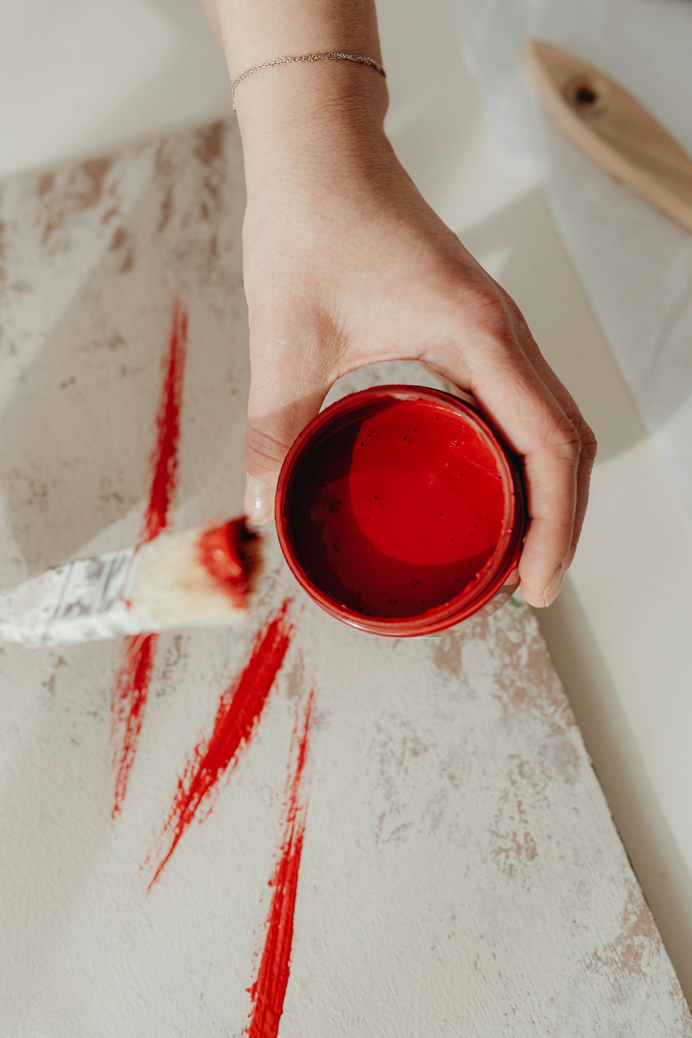 Close-up of a hand holding a red paint can with brush on canvas. Ideal for art and DIY concepts.