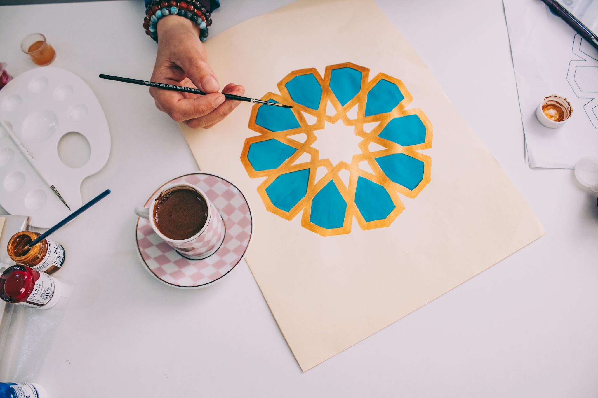 Top view of hand painting mandala with a coffee cup nearby, vibrant colors.